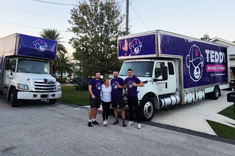 Happy customer after a move with Teddy Moving's team in front of two Teddy Moving & Storage trucks